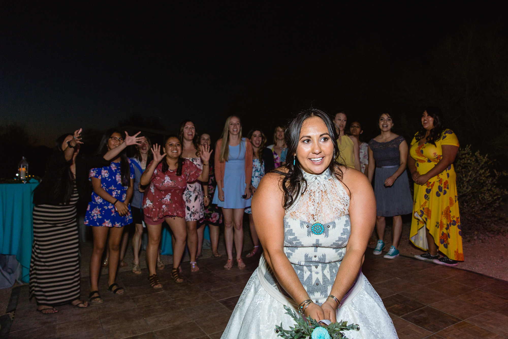 Bride tossing the bouquet to all the single ladies at her wedding reception by PMA Photography.