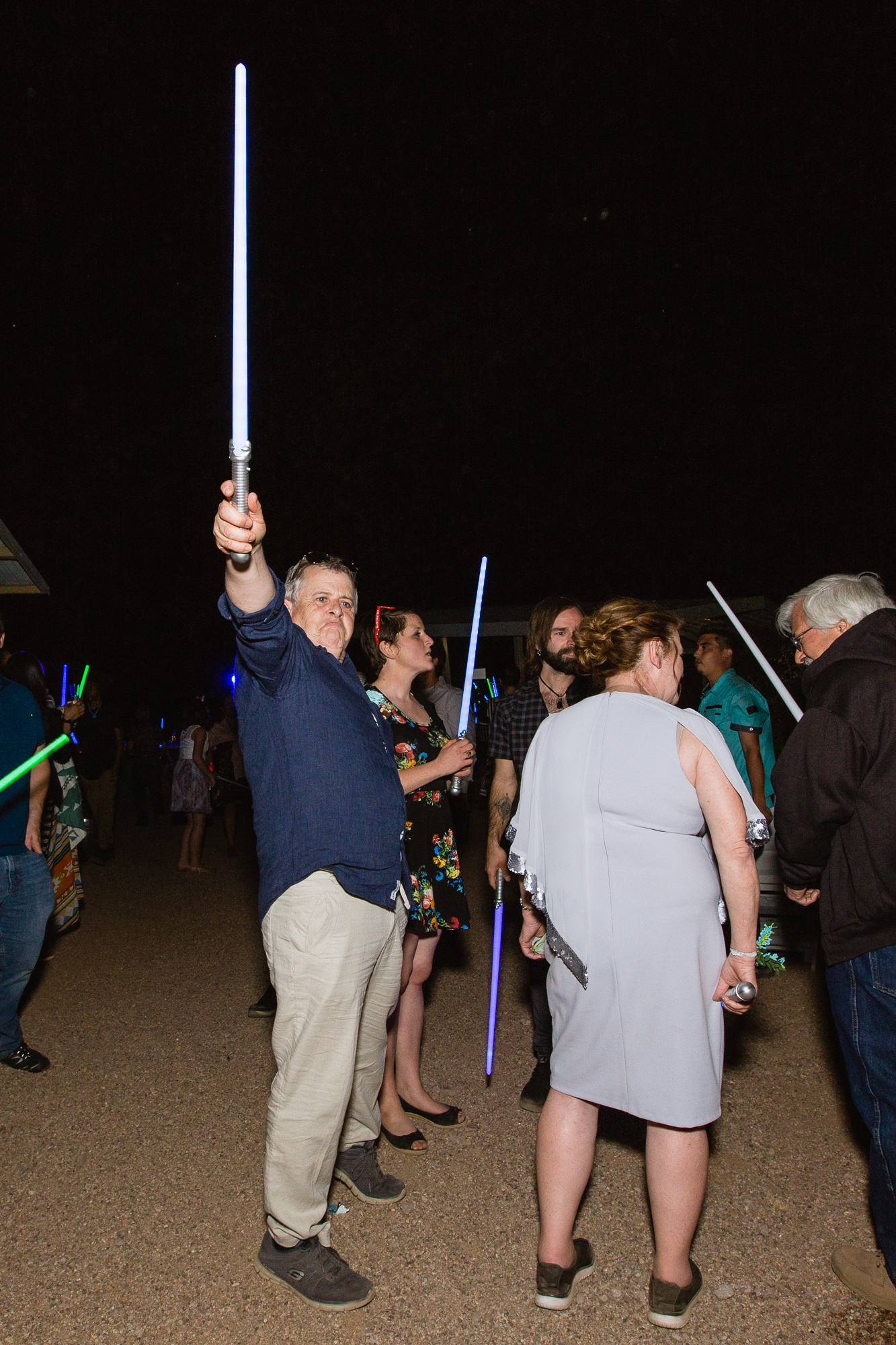 Father of the groom holding a lightsaber at a wedding reception by wedding photographer PMA Photography.