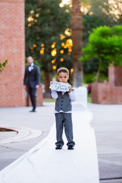 Ring bearer holding a Hear Comes the Bride sign by Phoenix wedding photographer PMA Photography.