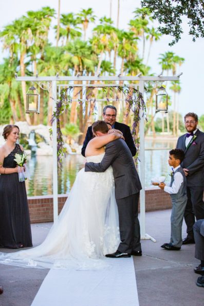 Bride and groom share their first kiss during their wedding ceremony at Encanto Park by Arizona wedding photographer PMA Photography.