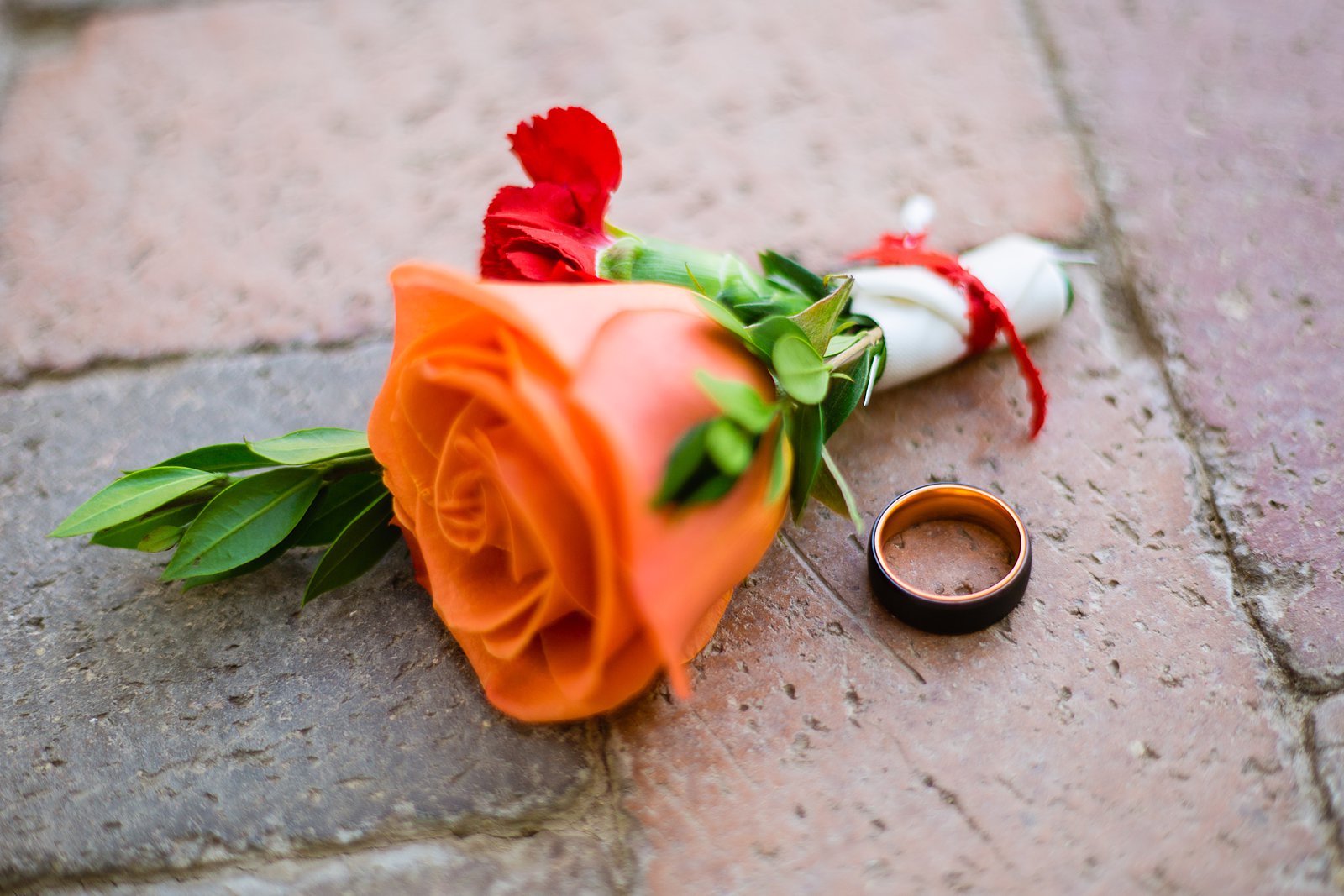 Groom's colorful orange and red rose boutonniere and black and orange Manly Bands wedding ring by PMA Photography.