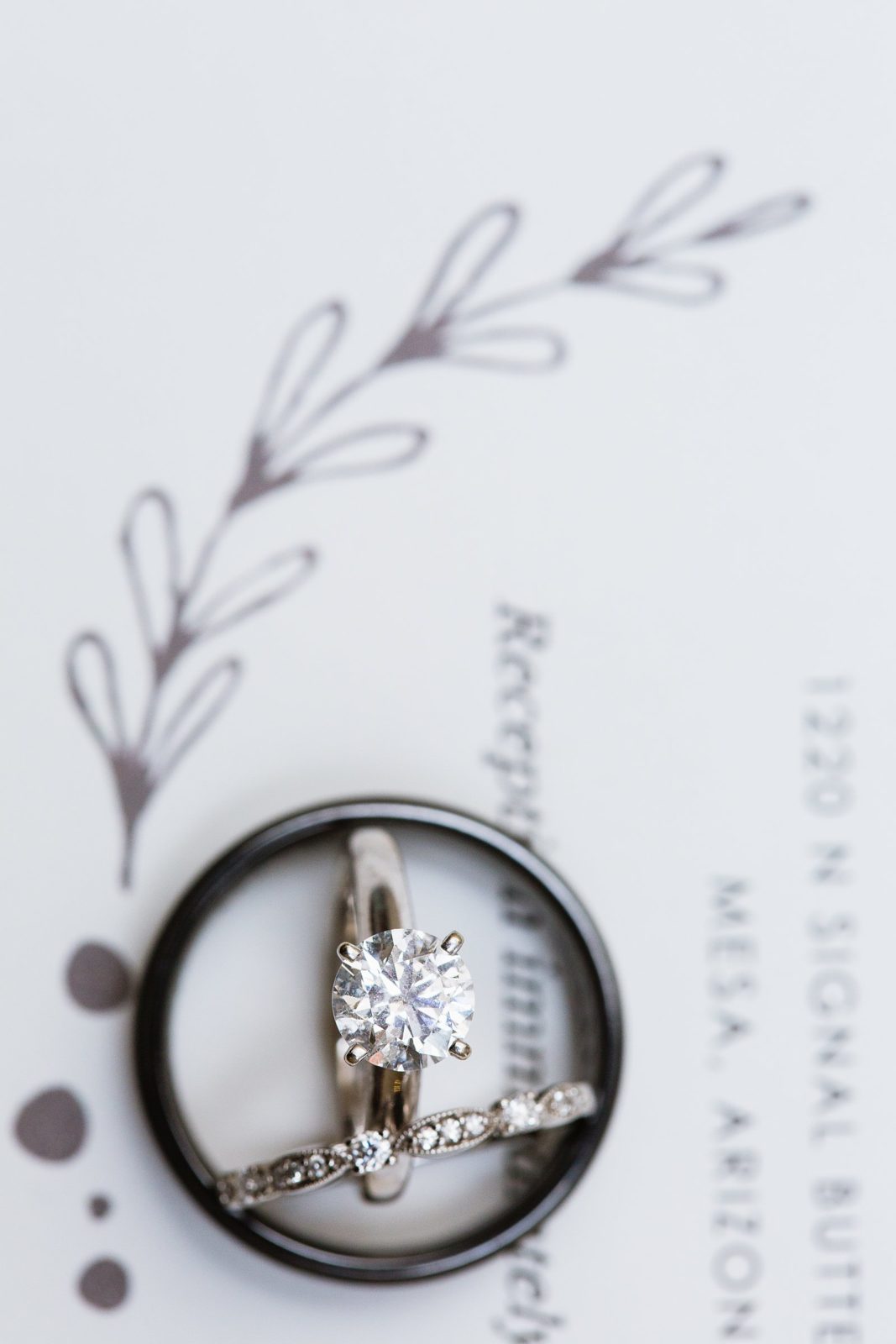 Simple white gold and black wedding bands on botanical invitation by PMA Photography.