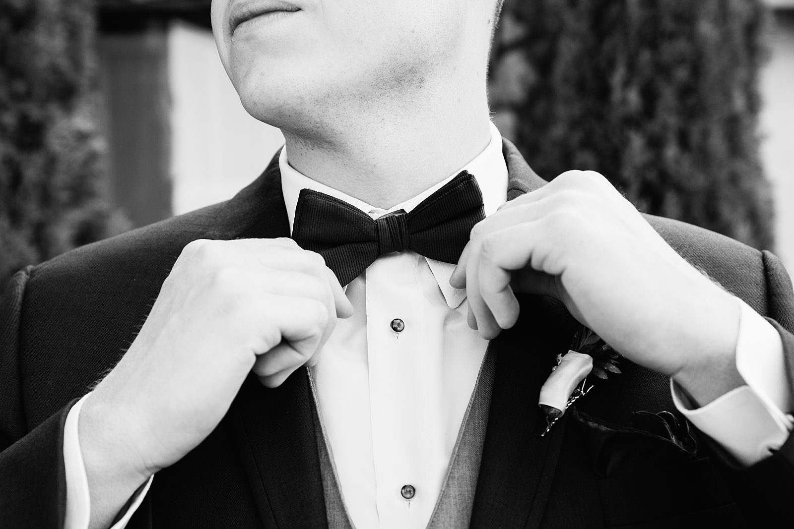 Black and white image of a groom adjusting his bowtie while getting ready for his wedding day by PMA Photography.
