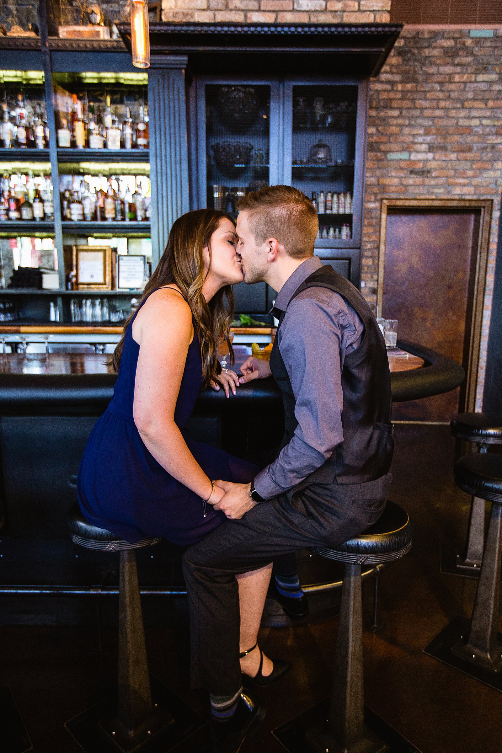Couple share a kiss during their Downtown Phoenix bar engagement session by Phoenix wedding photographer PMA Photography.