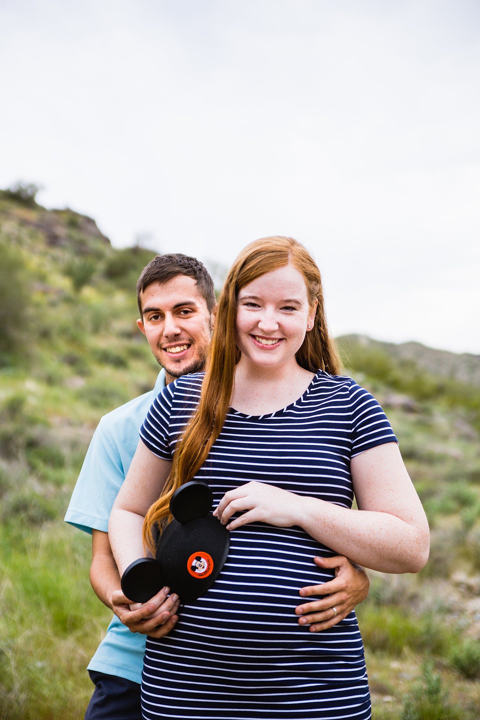 Couple pose with a set of baby mickey mouse ears for their Pima Canyon maternity session by Phoenix wedding photographer PMA Photography.