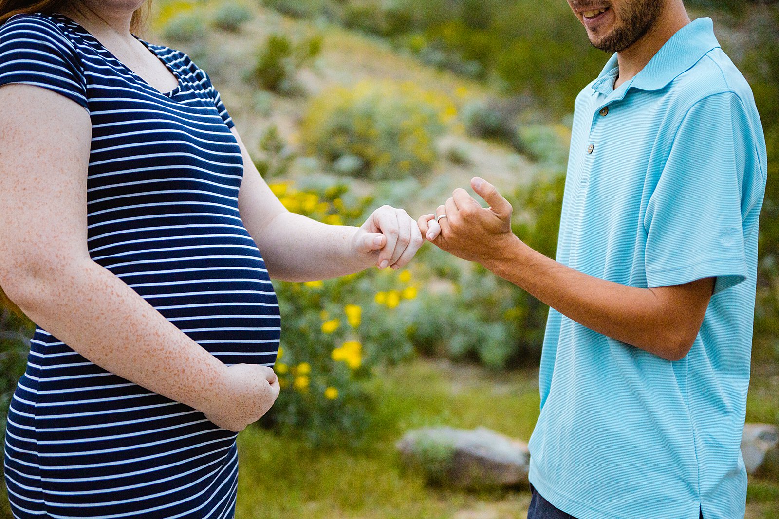Close up image of couple doing a pinkie promise with a baby bump by PMA Photography.