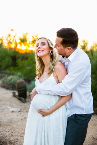 Pregnant bride and Groom laughing together during their desert backyard elopement in Scottsdale by Arizona wedding photographer PMA Photography.