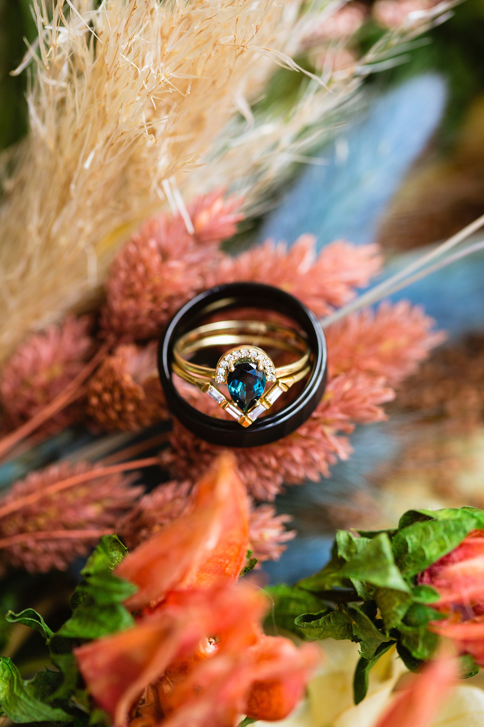 Unique emerald wedding ring set on top of peach and navy dried floral bridal bouquet by Phoenix wedding photographer PMA Photography.