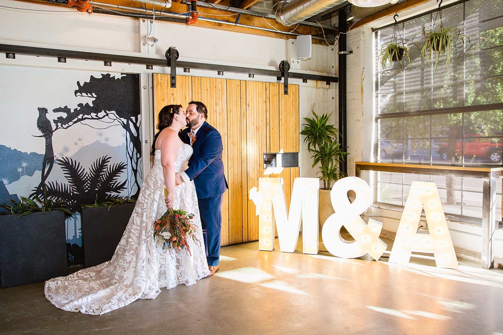 Bride and Groom share a kiss in front of light up letters of their initials during their MonOrchid wedding by Arizona wedding photographer PMA Photography.