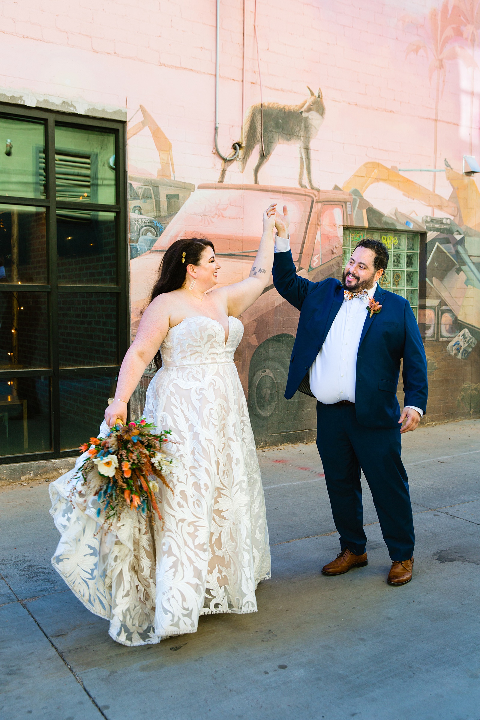 Groom twirling bride in front of a blush mural during their MonOrchid wedding by Arizona wedding photographer PMA Photography.