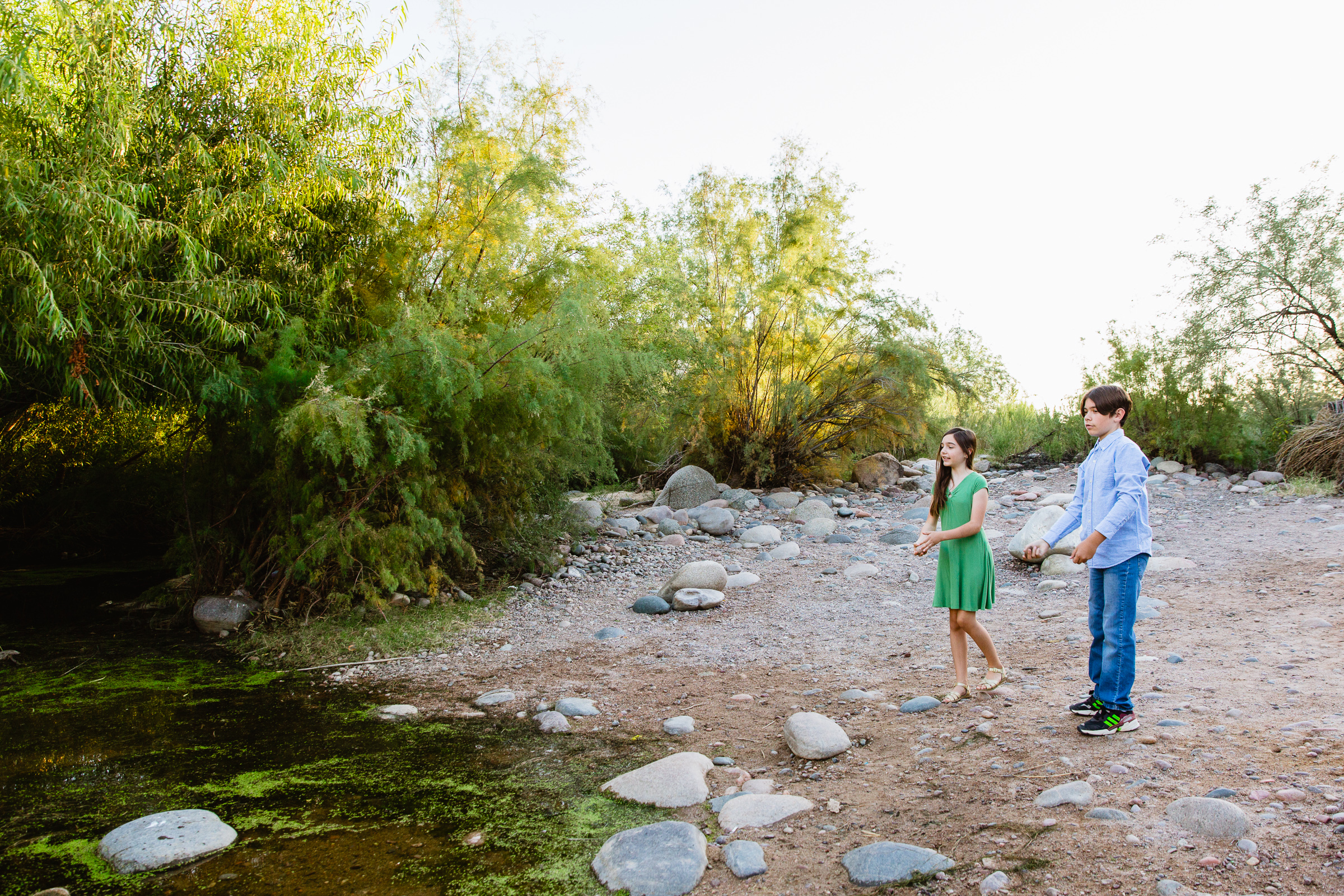 Kids having fun together skipping rocks at their Salt River family session by Phoenix family photographer PMA Photography.