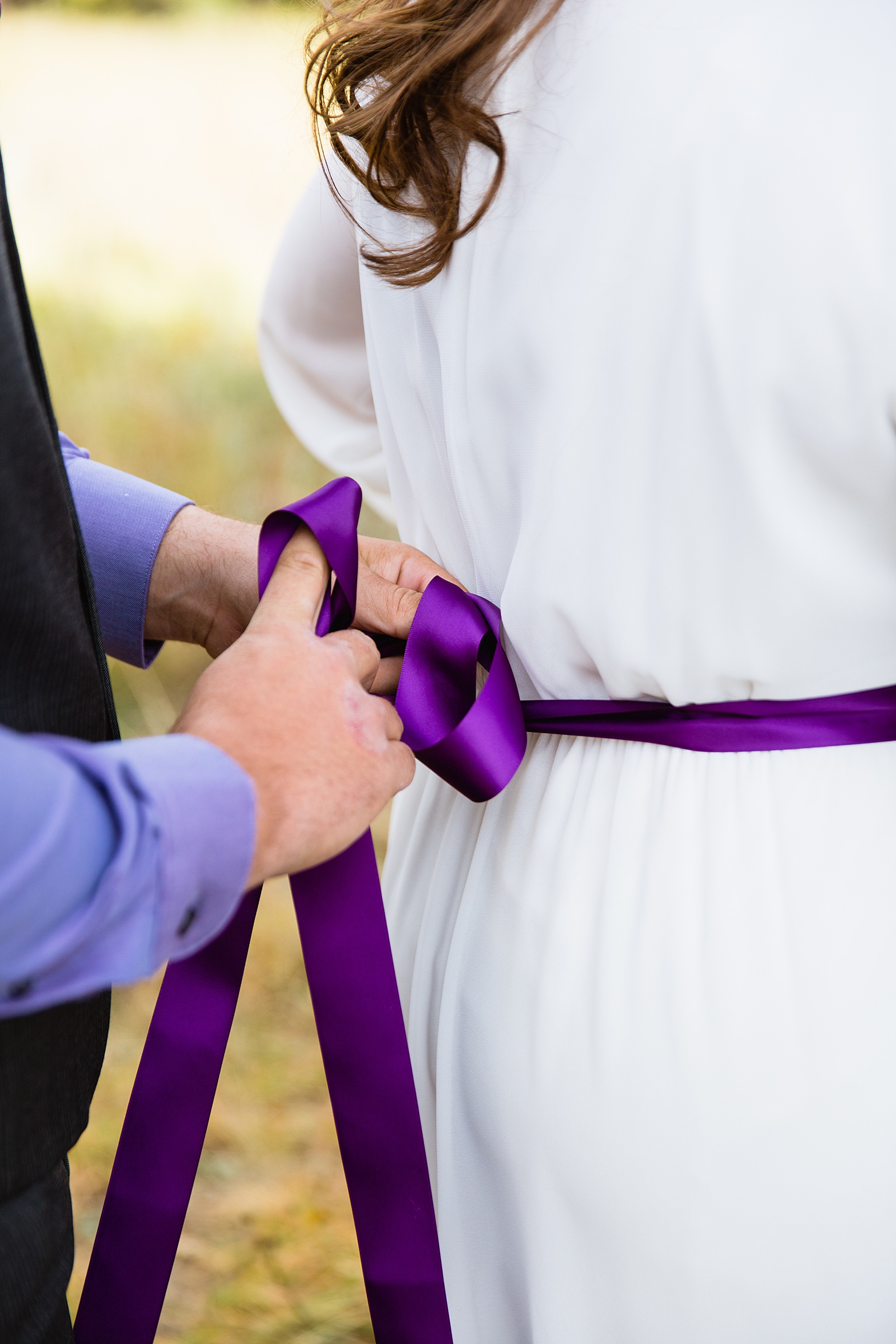 Groom helping the bride tie on her purple sash while getting ready for their elopement by Arizona elopement photographers PMA Photographer
