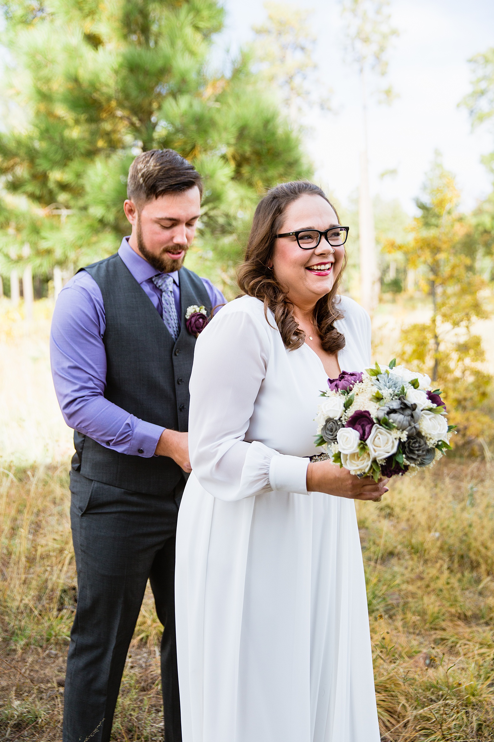 Bride laughing as the groom helps her tie on her purple sash while getting ready for their elopement by Arizona elopement photographers PMA Photographer