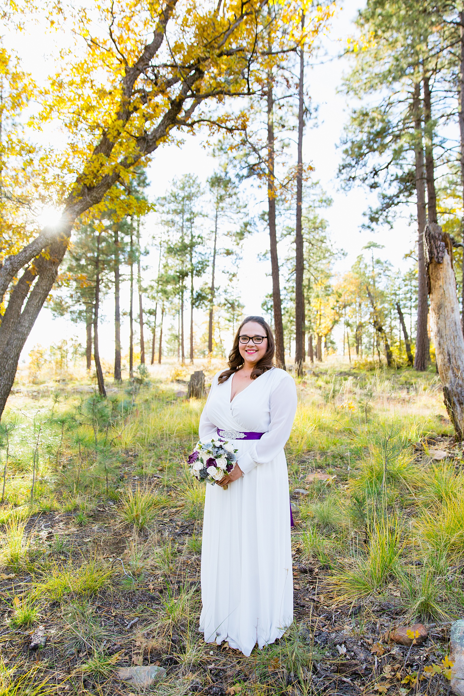 Bride's simple, sleeved wedding dress with a purple sash and wooden floral bouquet for her Mogollon Rim elopement by PMA Photography.