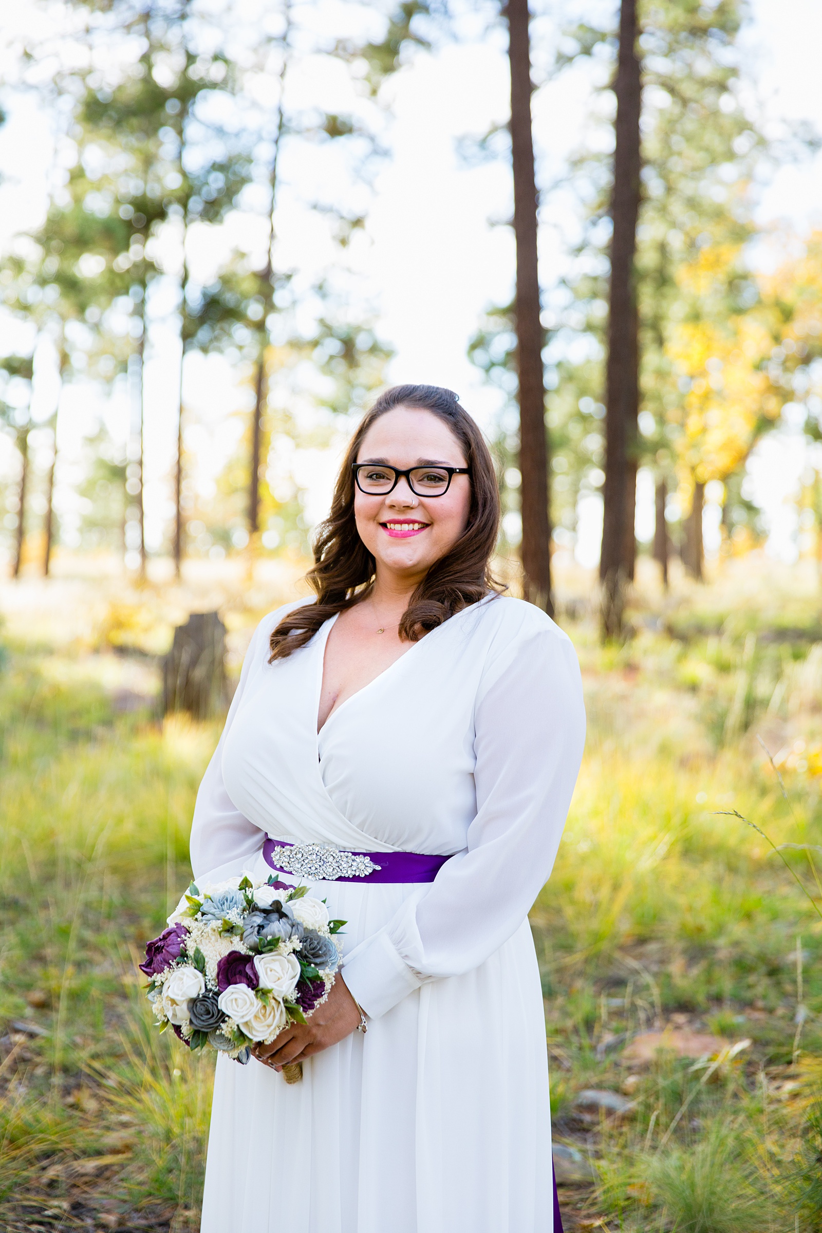 Bride's simple, sleeved wedding dress with a purple sash and wooden floral bouquet for her Mogollon Rim elopement by PMA Photography.