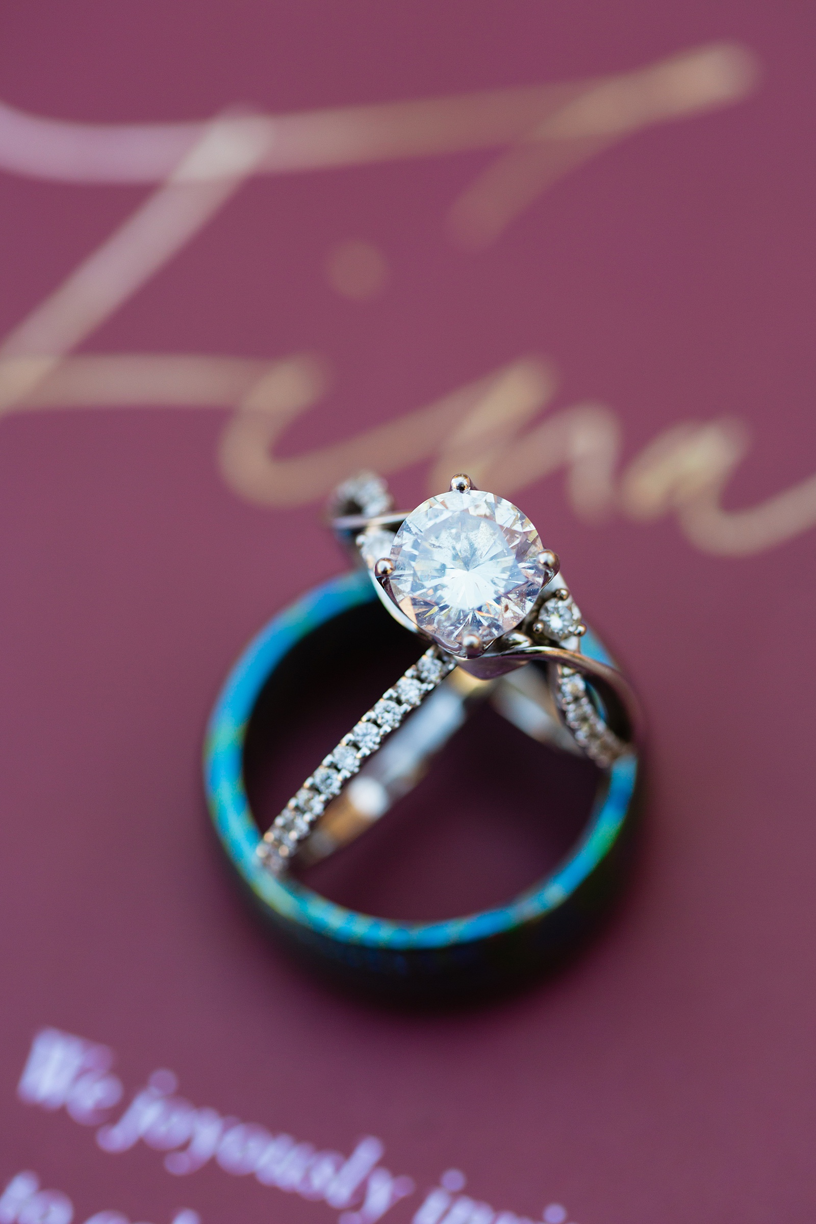 Wedding rings on top of maroon invitations by Phoenix wedding photographer PMA Photography.
