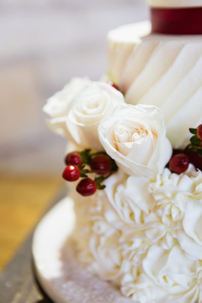 White and red wedding cake with white roses and red berries by Arizona wedding photographer PMA Photography.
