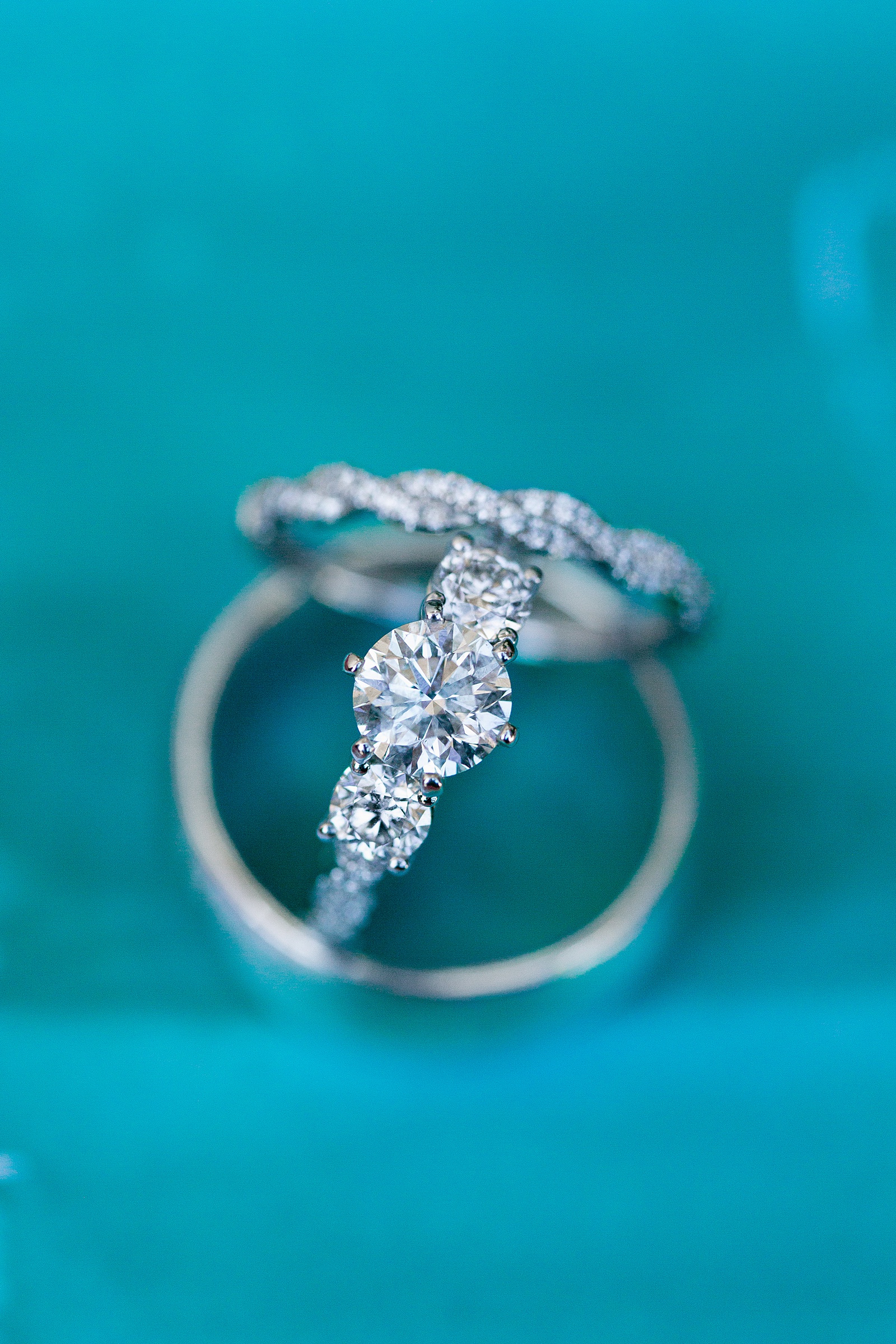 Three diamond white gold engagement ring stacked with his and her wedding bands on a blue backdrop by Arizona wedding photographer PMA Photography.