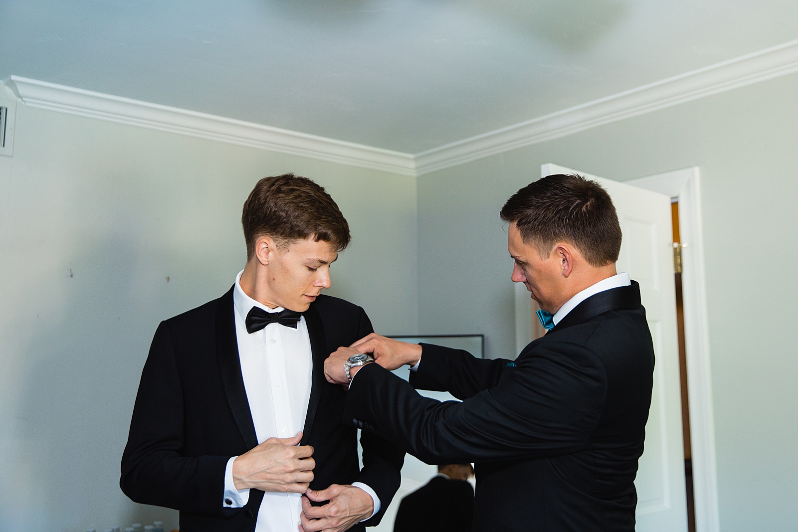 Groom helping a groomsmen with a pocket square while getting ready for the wedding day by Phoenix wedding photographer PMA Photography.