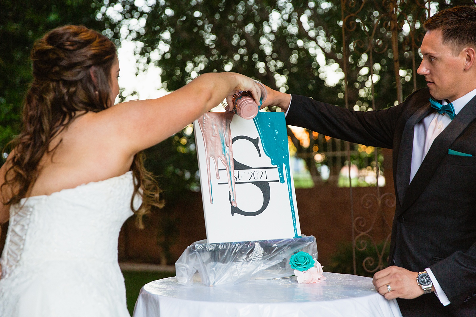 Unique unity ceremony of a paint pouring during a wedding ceremony. The couple pours different color paints onto the canvas and removed the sticker to create a custom piece of art for their home. Photograph by Arizona wedding photographer PMA Photography.