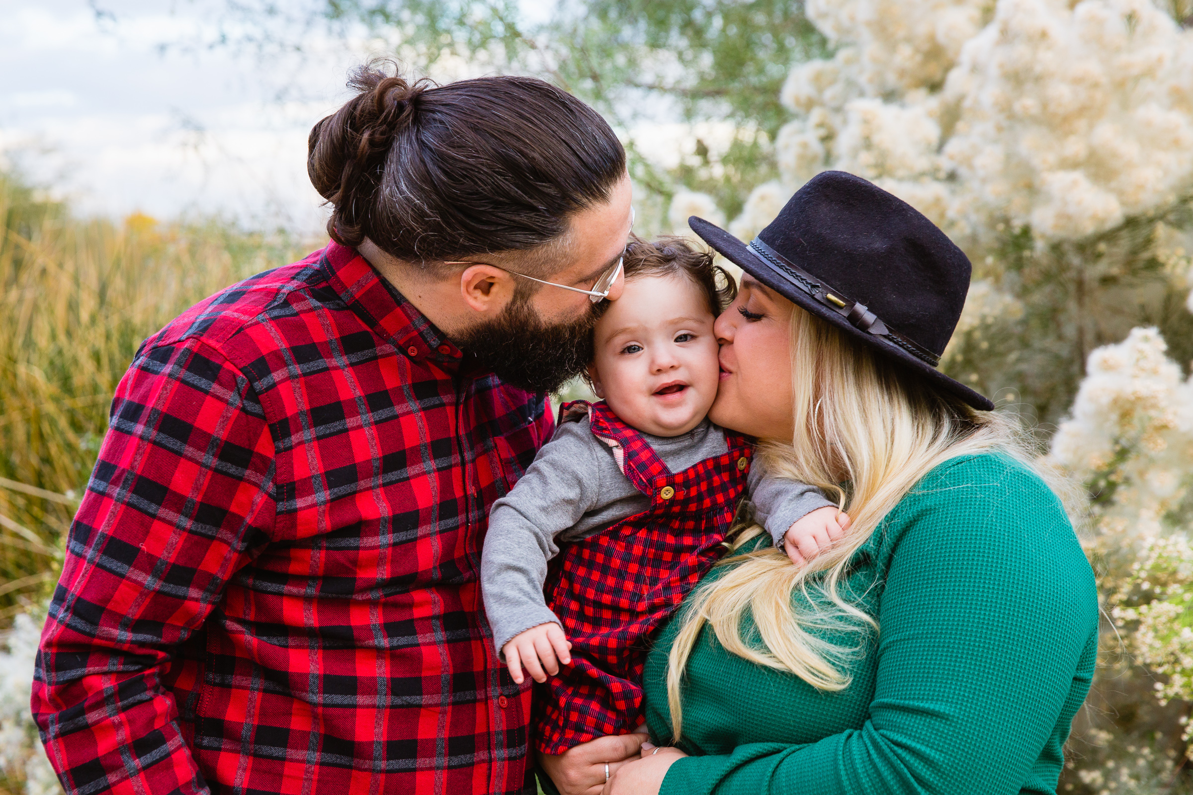 Parents kiss their baby daughter on the cheek during their Gilbert family session by Arizona family photographer PMA Photography.