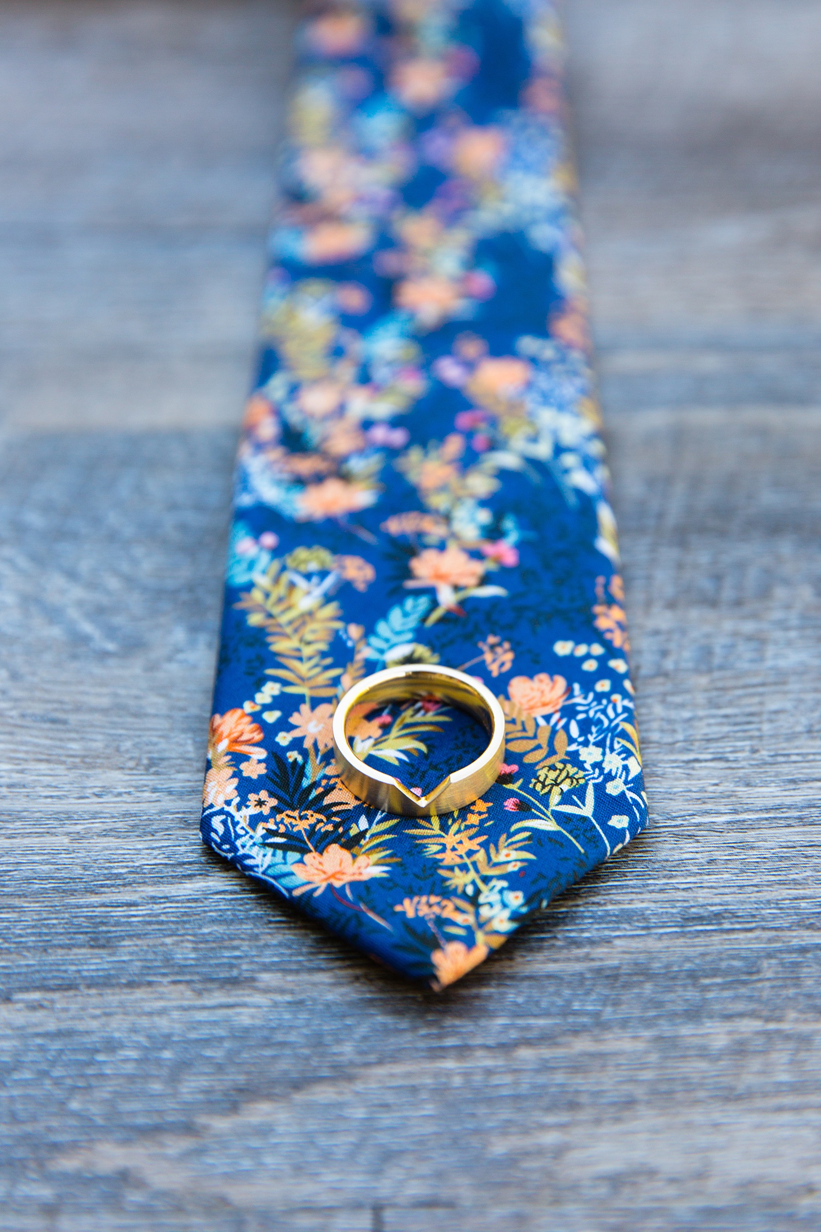 Groom's wedding day details of a floral tie and unique gold wedding ring by PMA Photography.