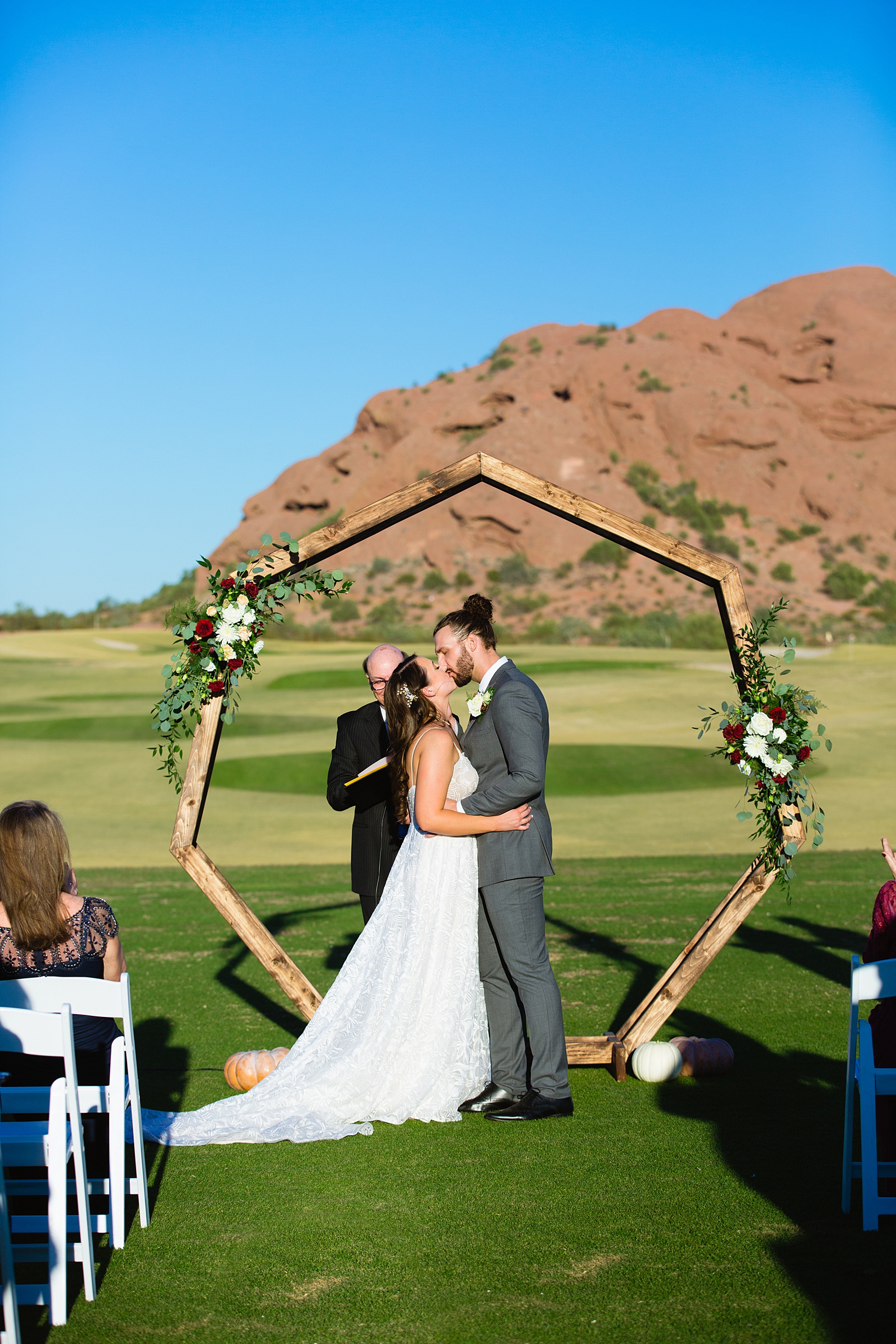 Bride and groom share their first kiss during their wedding ceremony at Papago Events by Arizona wedding photographer PMA Photography.