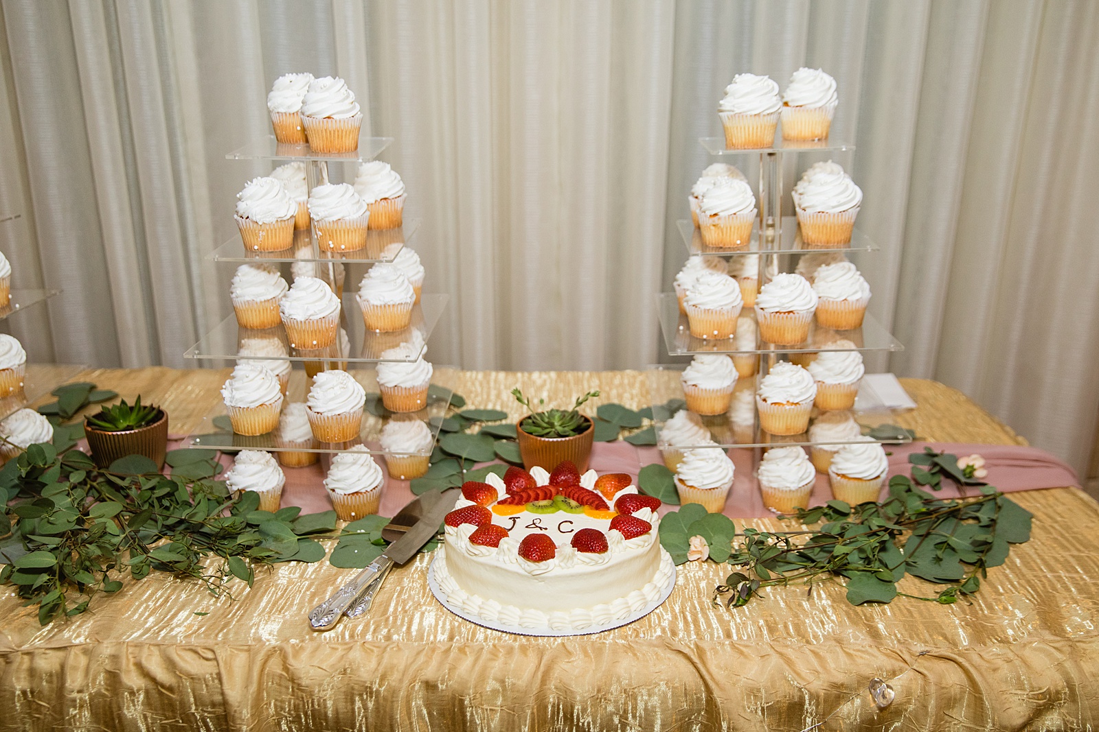 Simple wedding cake with fruit and white cupcakes on cupcake stands.