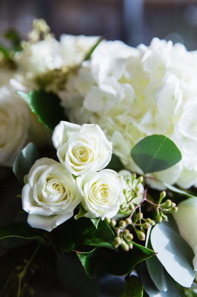 Close up image of a white rose floral arrangement at Clear acrylic, modern wedding table number with white flower and eucalyptus floral arrangement at a Troon north wedding reception by PMA Photography.
