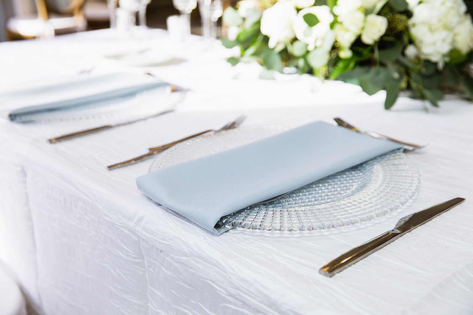 Modern white, clear, and light blue table setting at a Clear acrylic, modern wedding table number with white flower and eucalyptus floral arrangement at a Troon north wedding reception by PMA Photography.