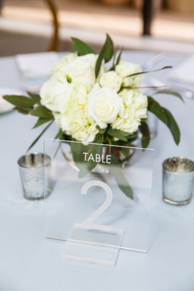 Clear acrylic, modern wedding table number with white flower and eucalyptus floral arrangement at a Troon north wedding reception by PMA Photography.