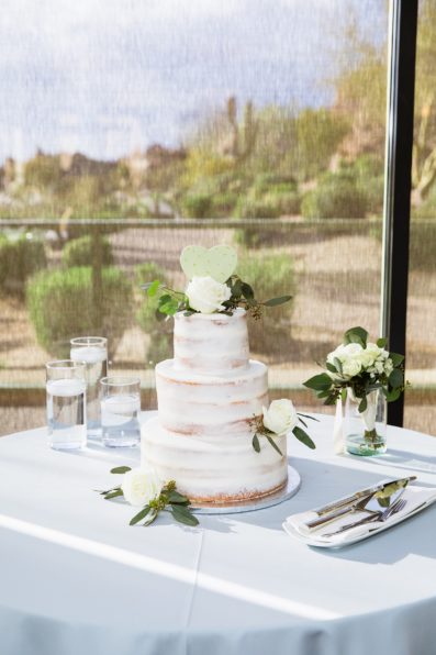 Simple white, three tiered wedding cake with rose and eucalyptus by PMA Photography.