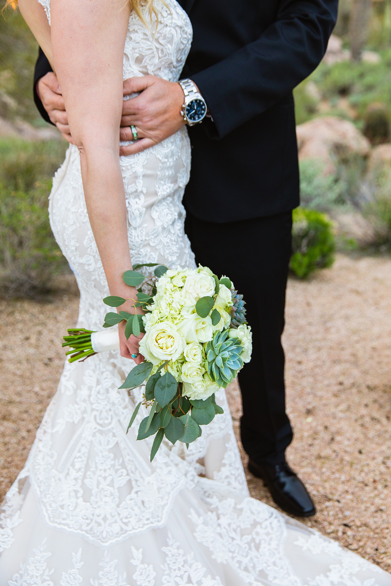 Bride holding a white and greenery wedding bouquet while her groom holds her at a Troon North wedding by Scottsdale wedding photographer PMA Photography.