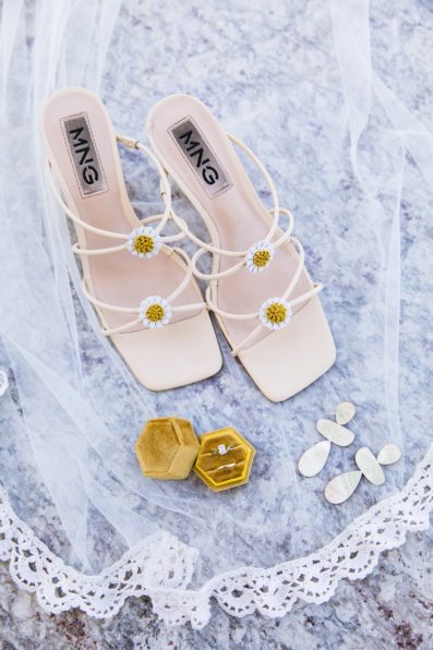Bride's wedding day details of her floral shoes, wood mid-century modern beespoke earrings, yellow hexagon ring box and wedding bands, and veil by PMA Photography.