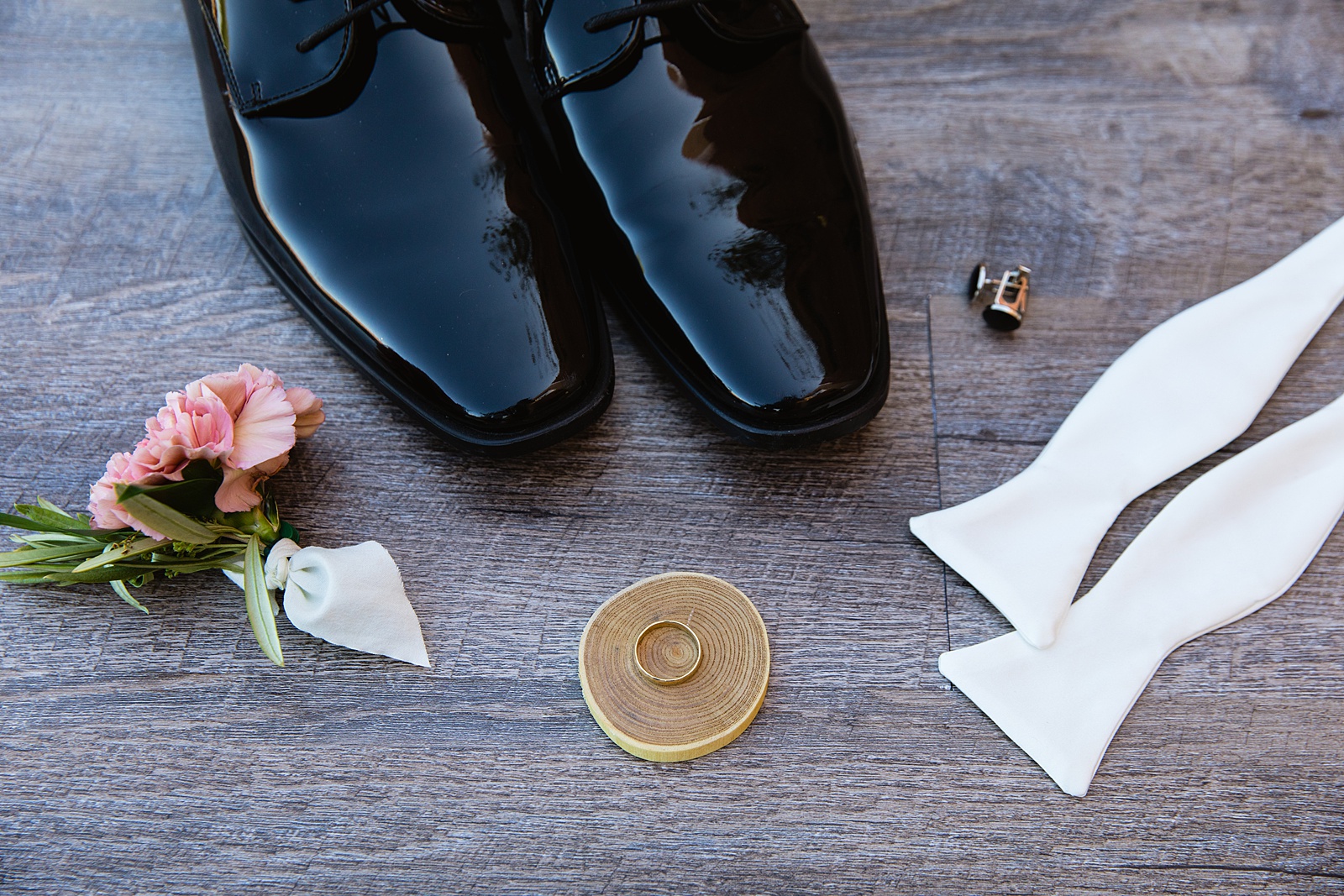 Groom's wedding day details of slick black shoes, boutonniere, cuff link and white tie by PMA Photography.