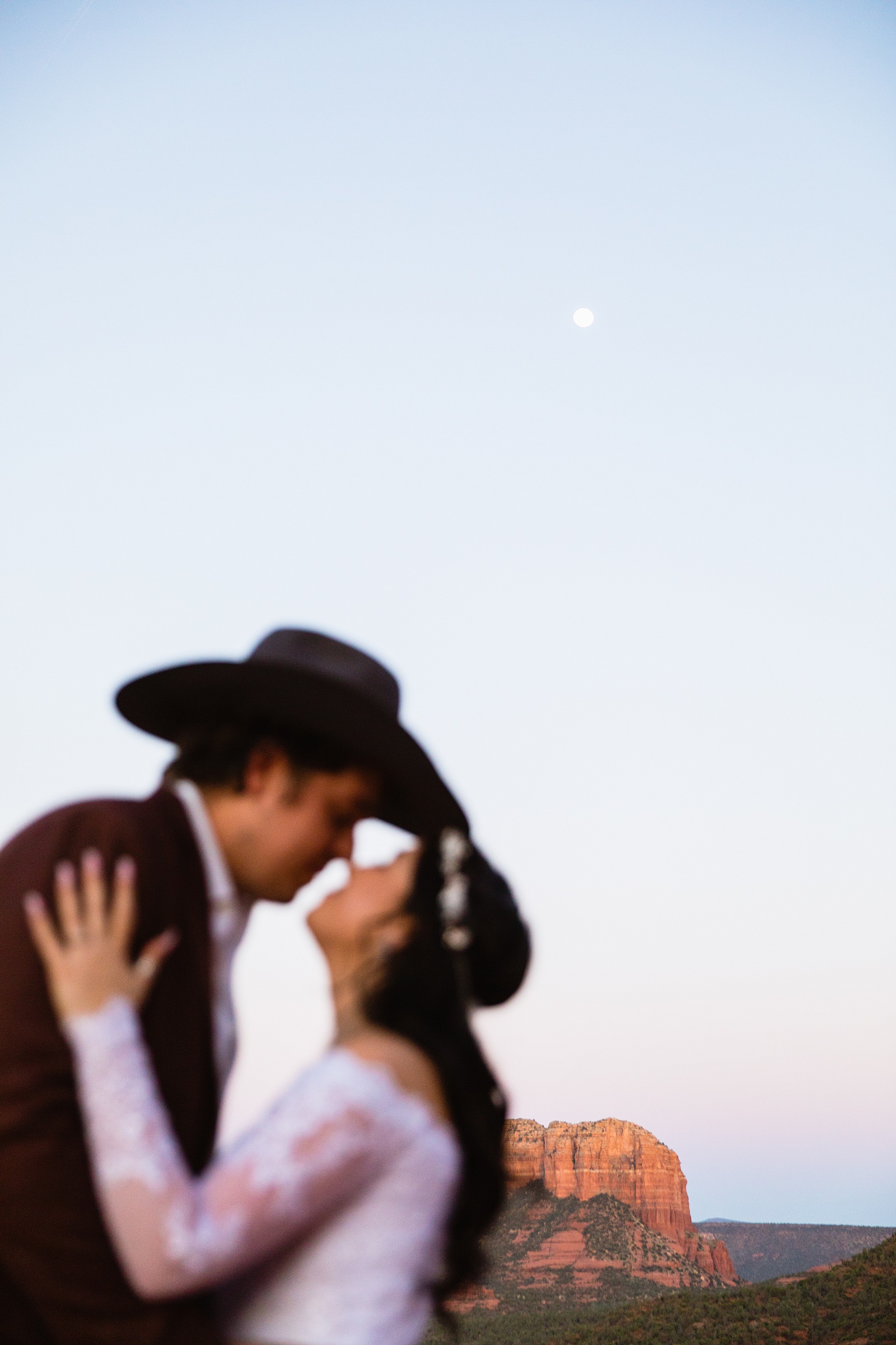Newlyweds kissing with the moon and Courthouse Vista behind them at their Sedona elopement by PMA Photography.