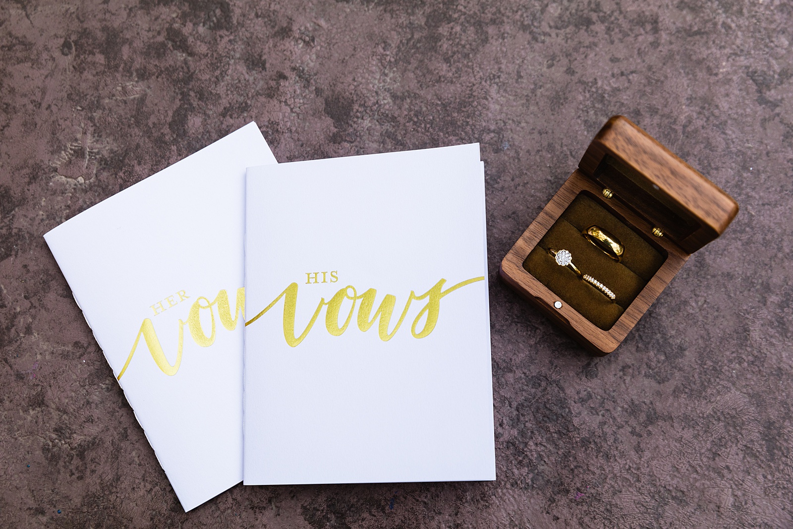 Couple's gold wedding rings with their white and gold vow books by PMA Photography.
