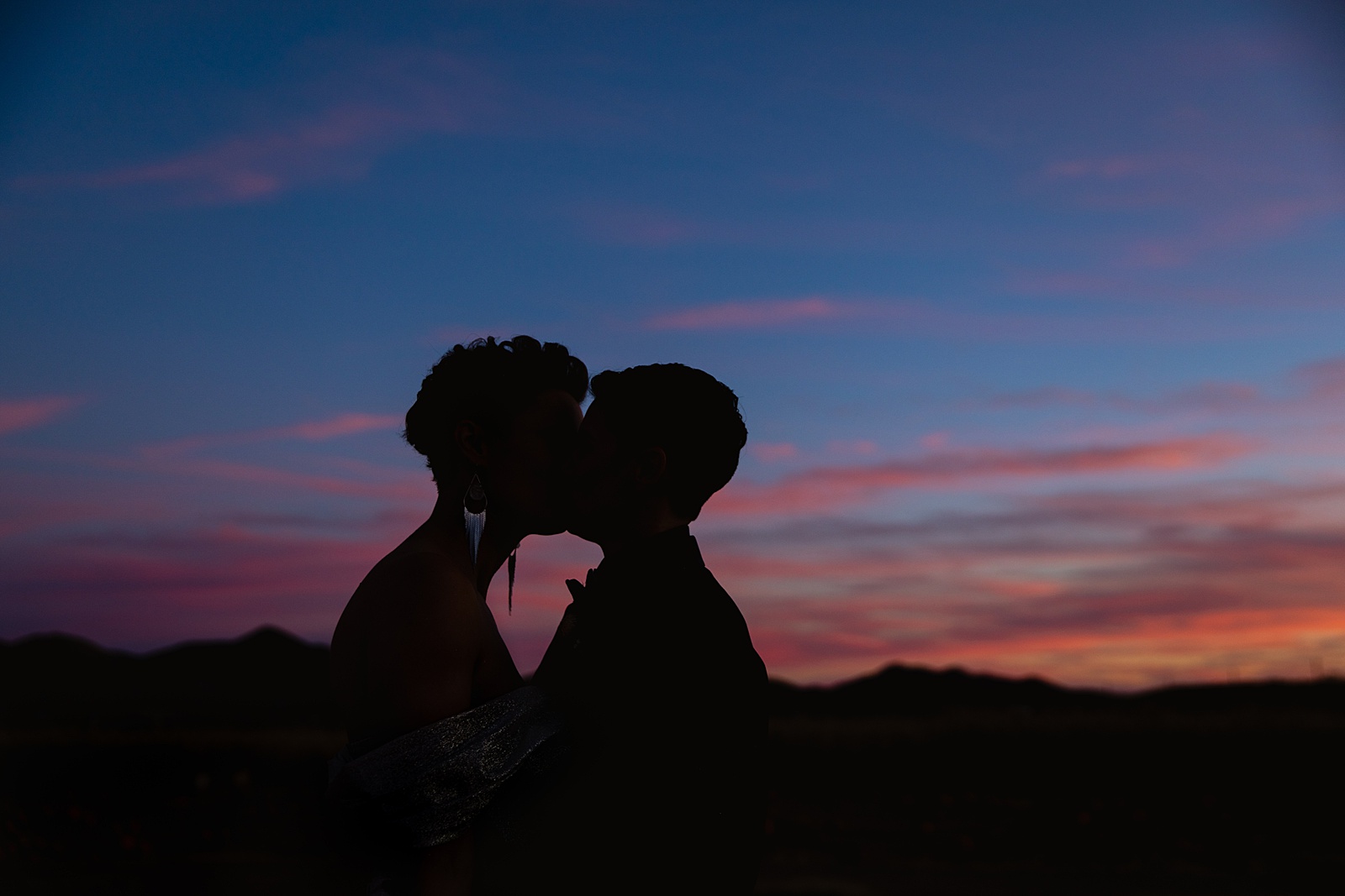 Same sex couple share a kiss at sunset during their Mortimer Farms wedding by Prescott wedding photographer PMA Photography.