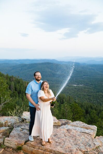 Adventurous couple popping champagne together during their Mogollon Rim engagement session by Payson engagement photographer PMA Photography.