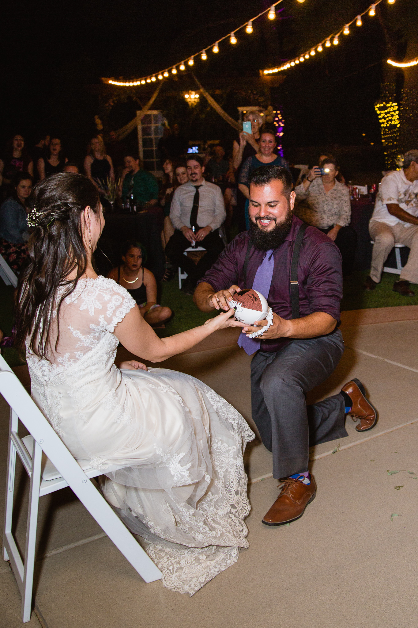 Groom putting garter on football for the garter toss by wedding photographer PMA Photography.
