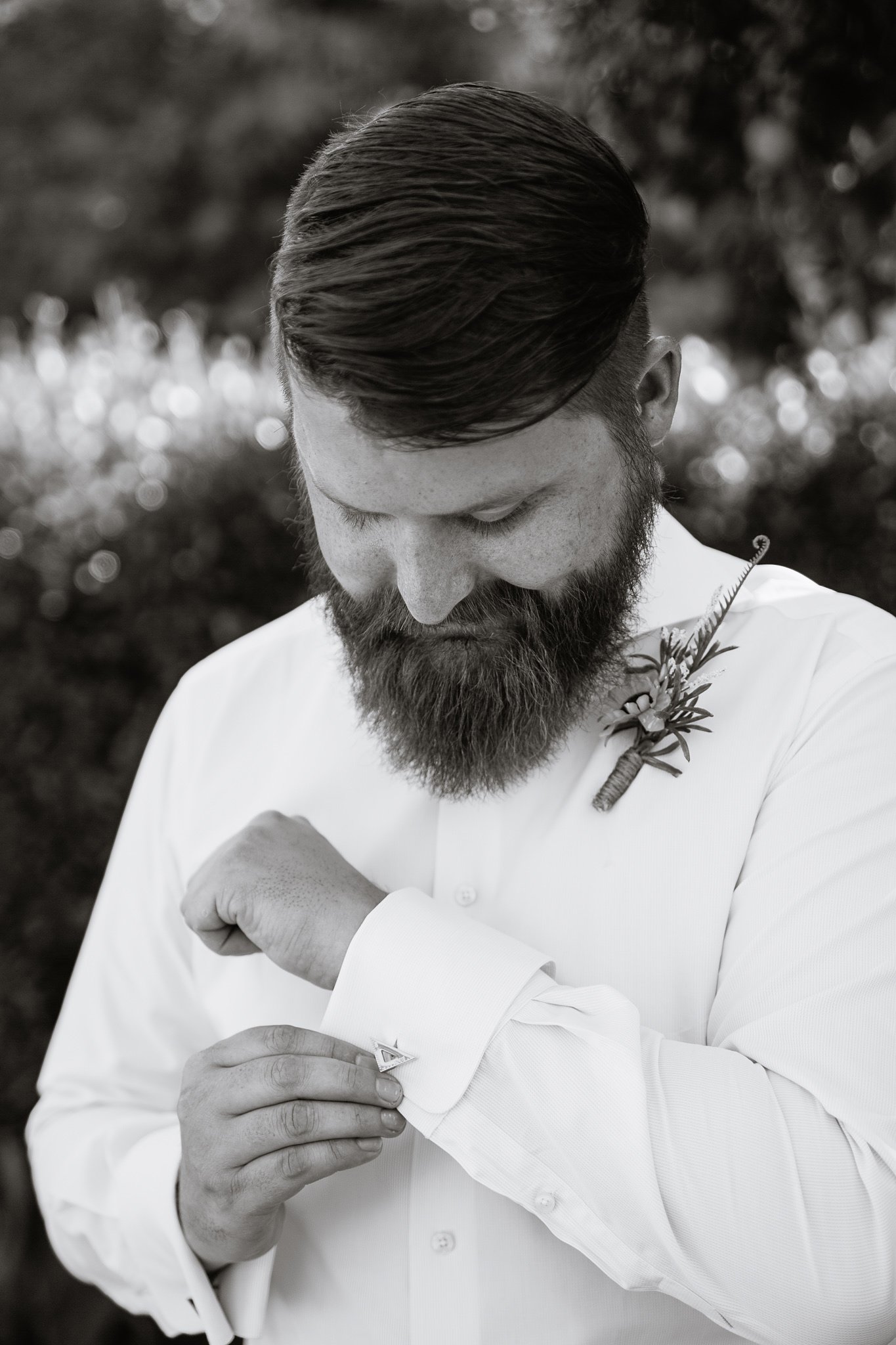 Black and white image of groom putting on custom cuff link while getting ready by Arizona wedding photographer PMA Photography. 