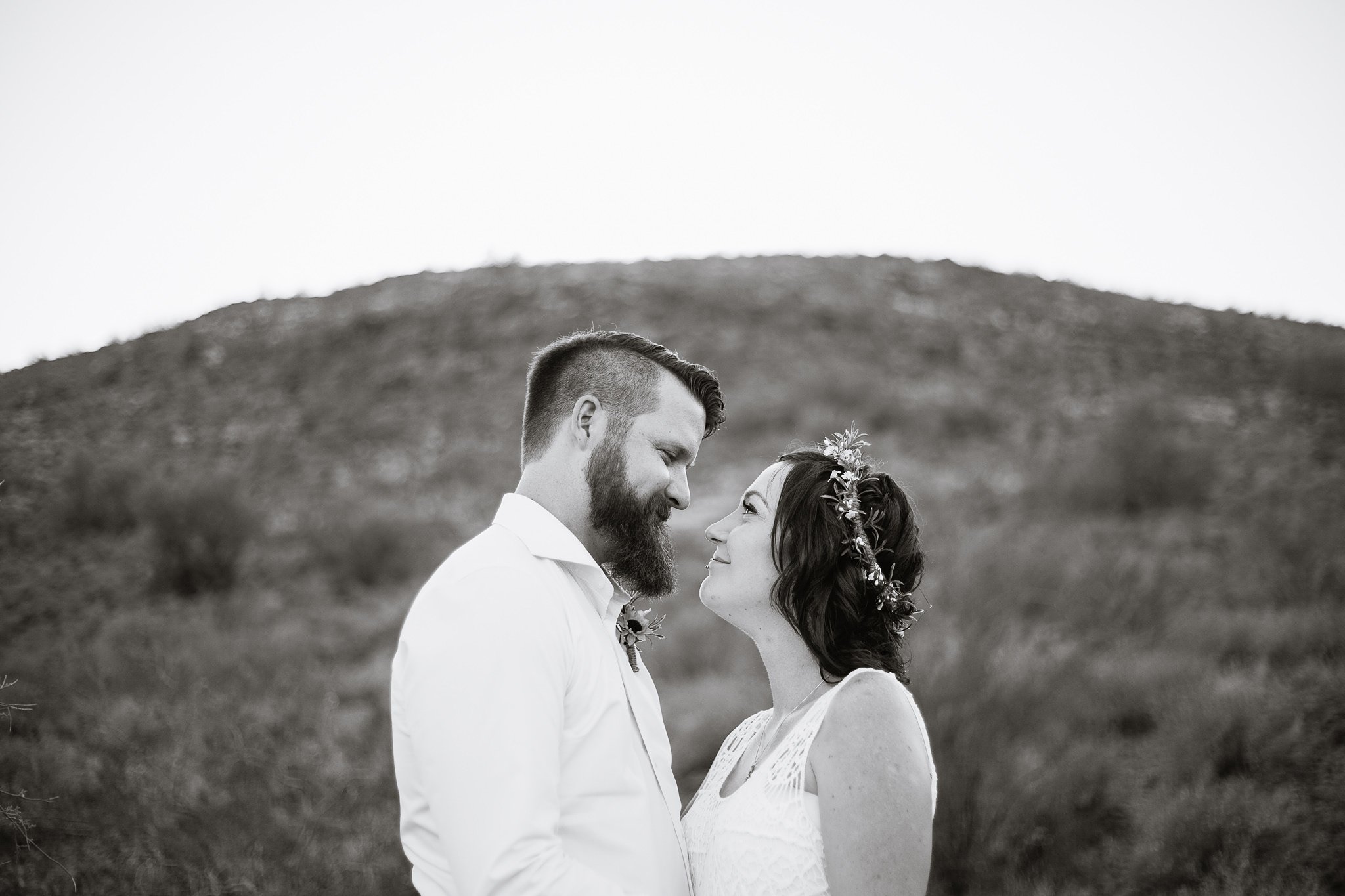 Black and white image of bride and groom looking at each other in front of small desert mountain by Phoenix wedding photographer PMA Photography.