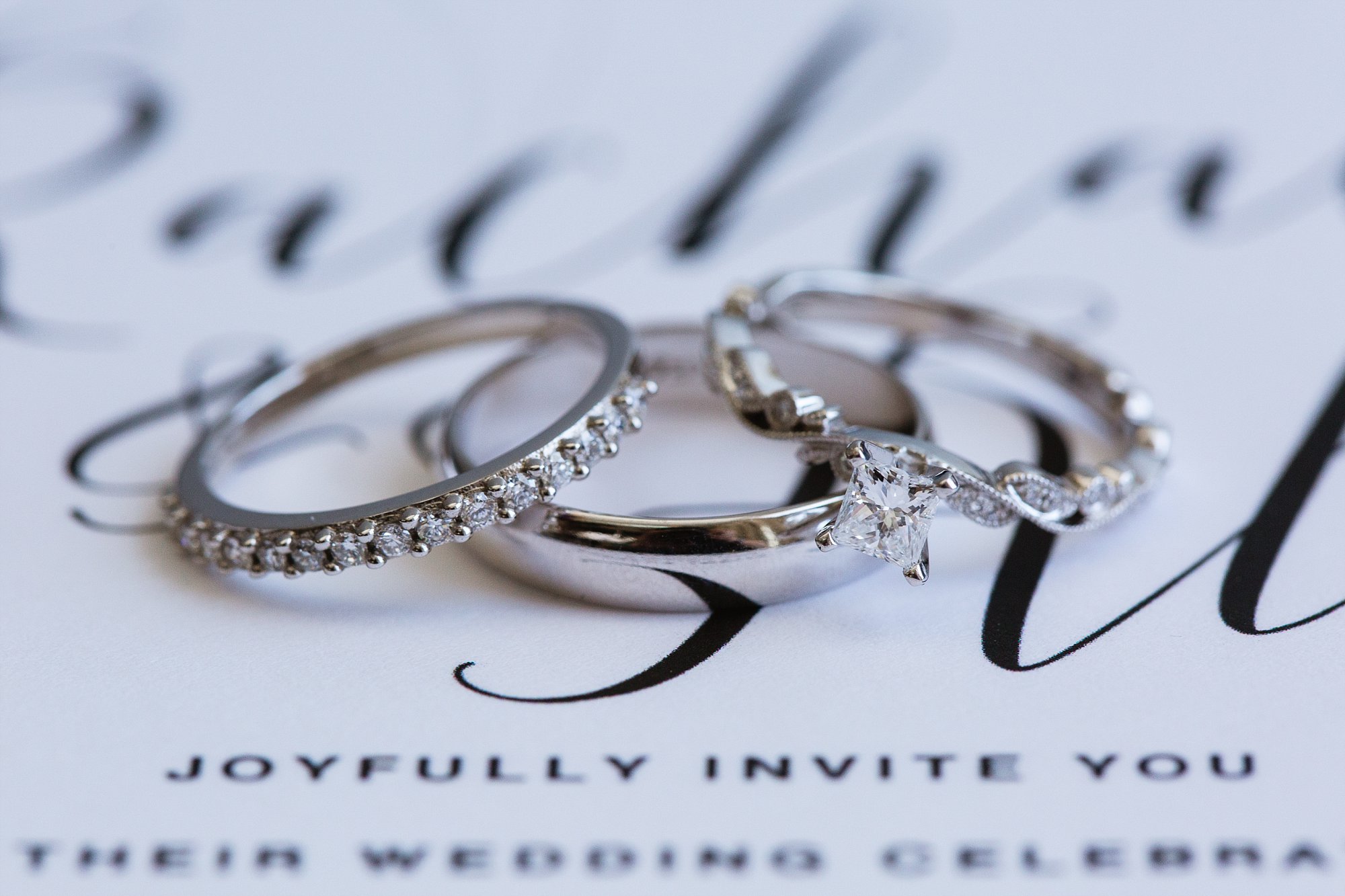 Close up image of bride and groom's wedding rings on their wedding invitation by wedding photographer Amber Kirchner of PMA Photography.