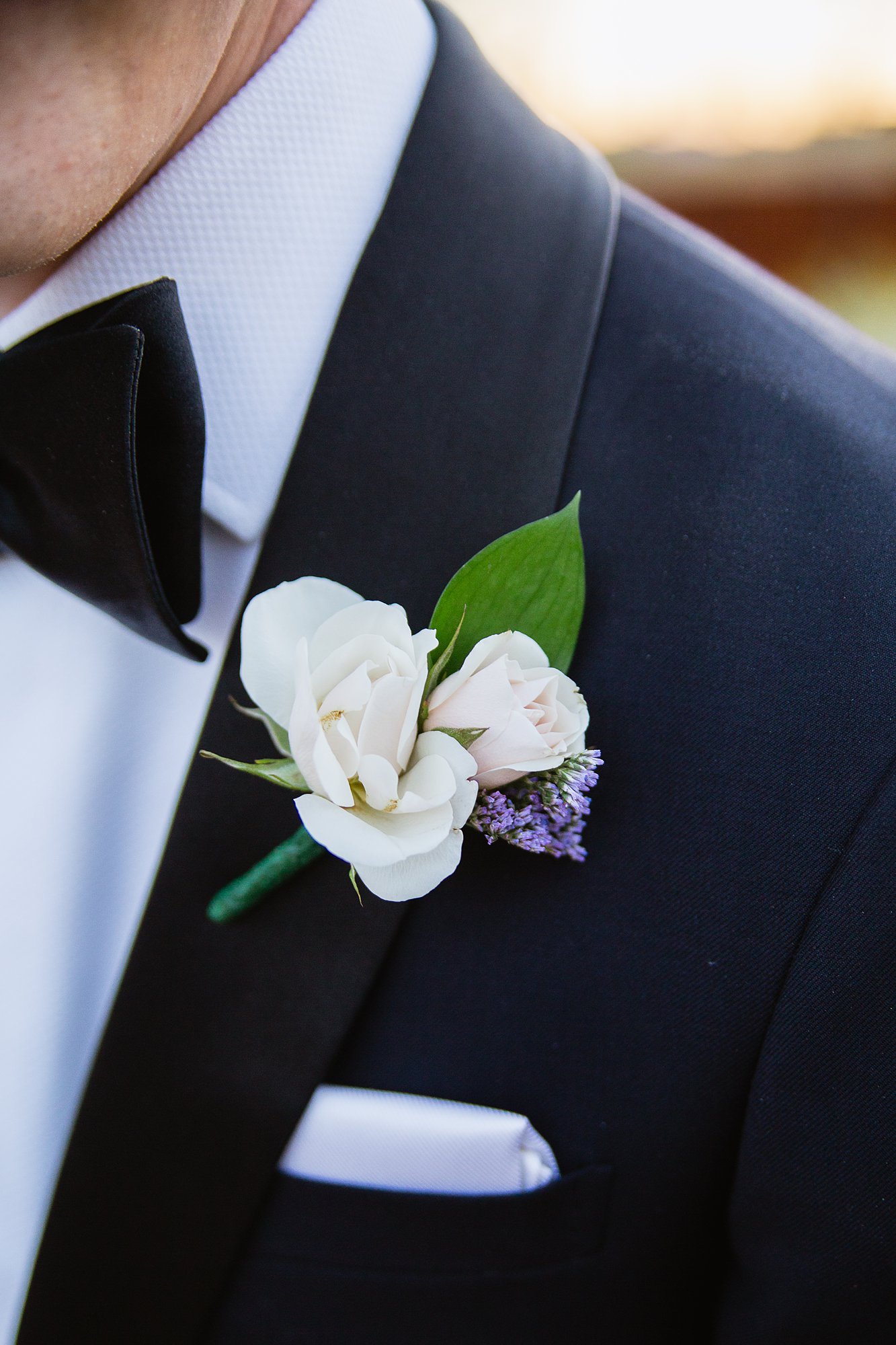 Close up image of a small rose boutonniere on a grooms custom made tux.
