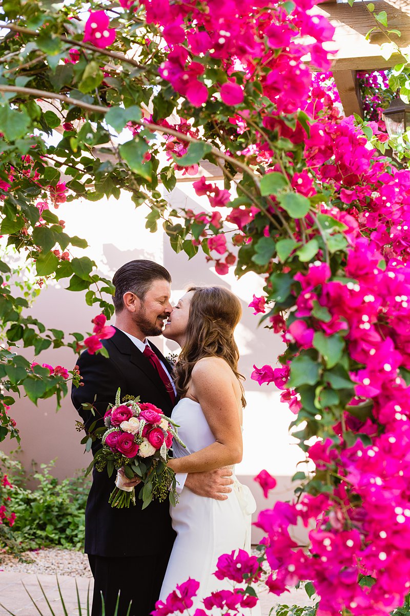 Bride and groom kiss behind pink bougainvillea plant at Hermosa Inn by Phoenix wedding photographer PMA Photography.