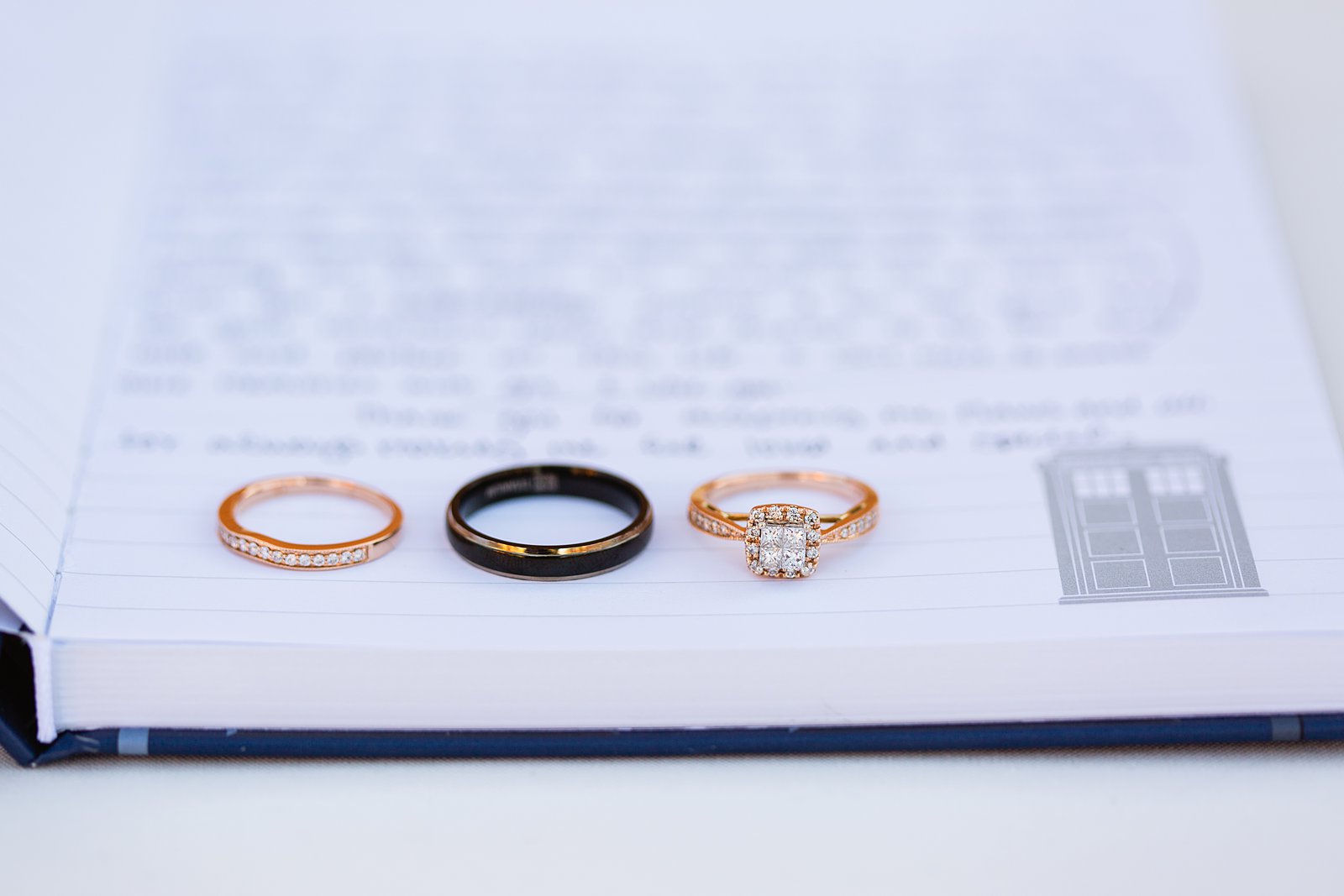 Bride and grooms rose gold and black wedding bands in a Doctor Who tardis book by PMA Photography.