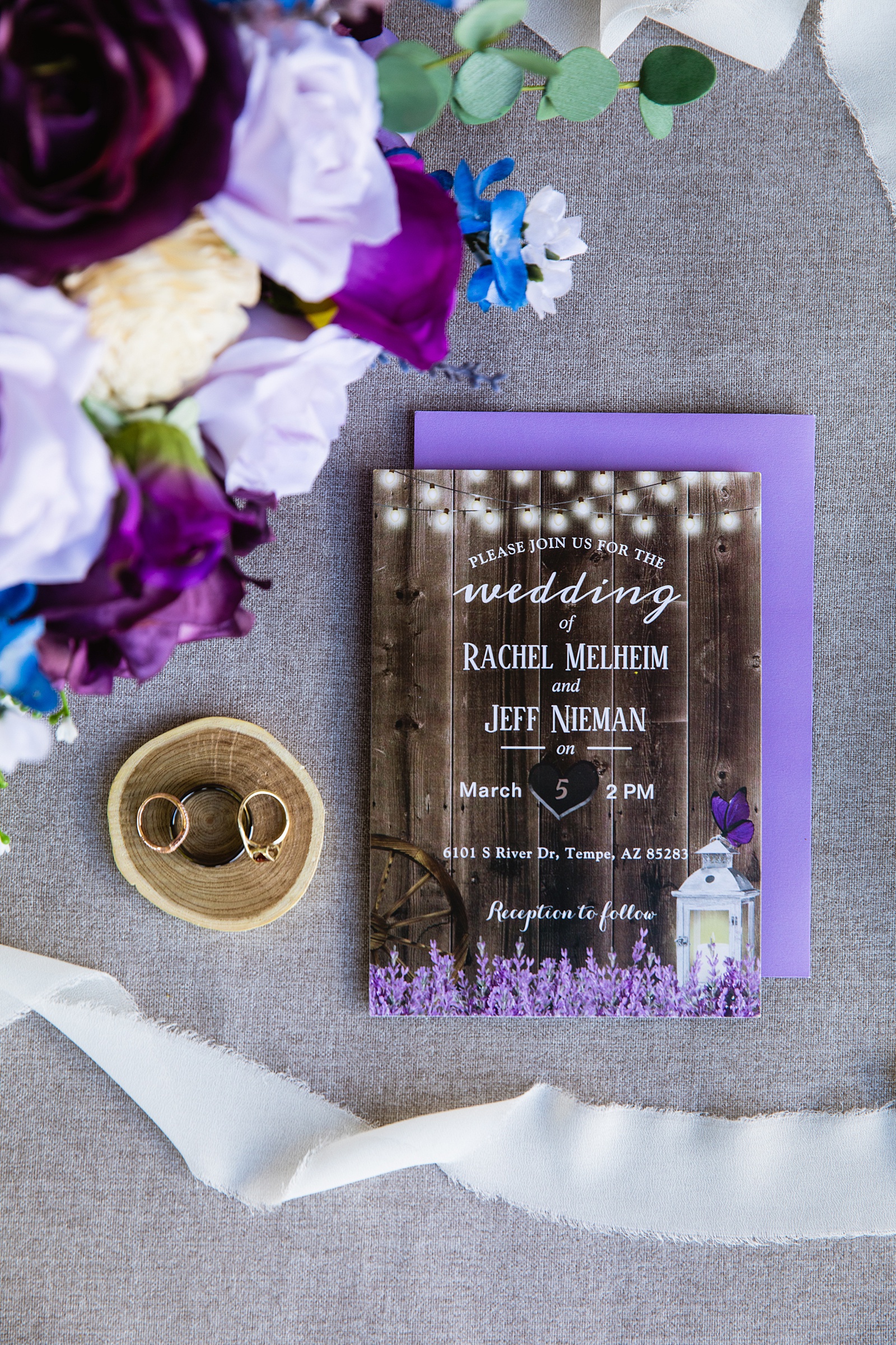 Bride and groom's wedding rings on top of a rustic and purple wedding invitations by PMA Photography.