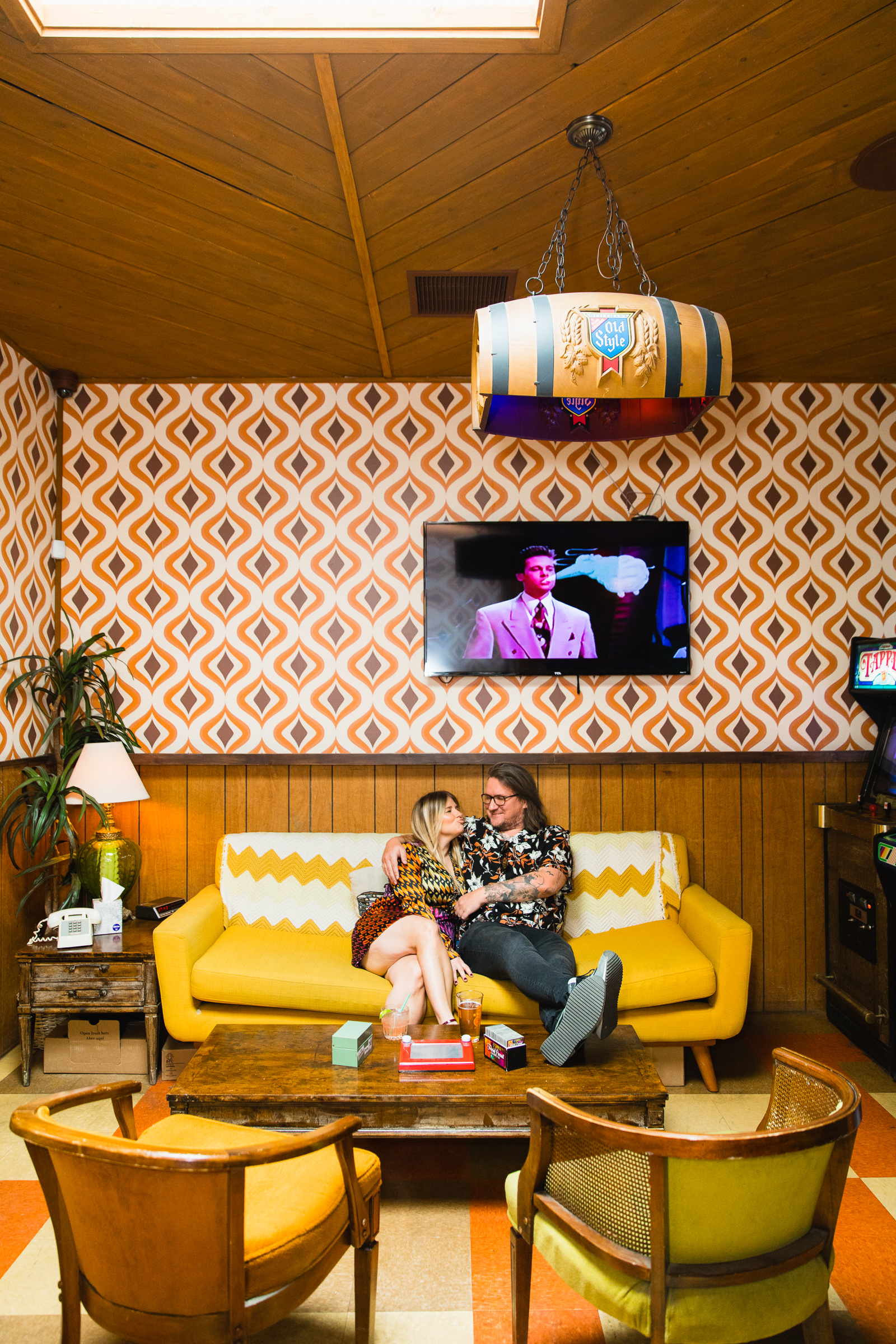 Couple having fun together on a funk yellow retro couch during their Thunderbird Lounge engagement session by Phoenix engagement photographer PMA Photography.