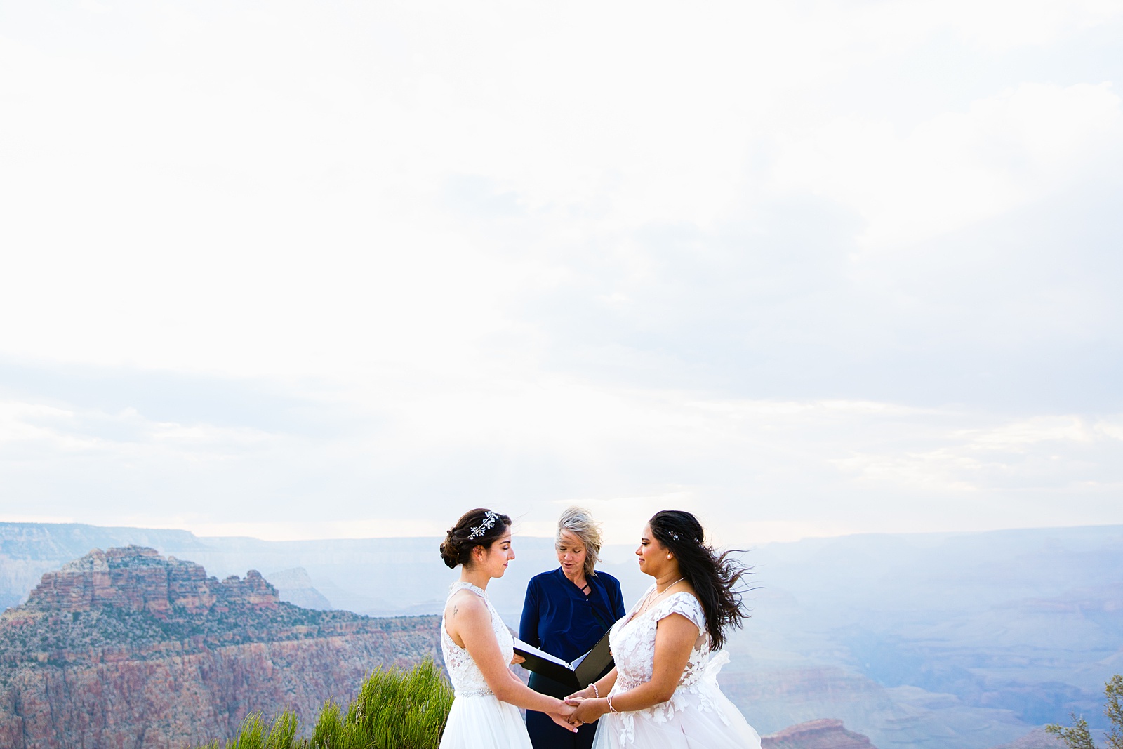 Two brides stand with their officiant during their marriage ceremony at the edge of the Grand Canyon by elopement photographer PMA Photography.