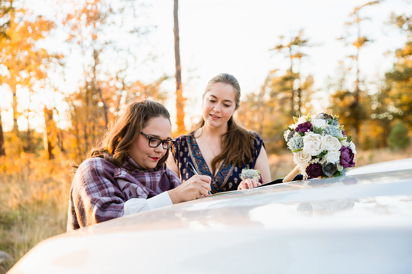 Bride signs her marriage license with her officiant and witnesses on the front of a truck during her fall elopement at the Mogollon Rim by PMA Photography.